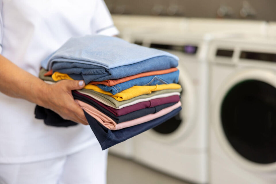 person holding pile of folded laundry near a line of washers